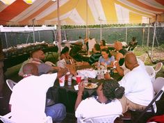 a group of people sitting around a table under a tent with food and drinks on it