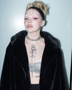 a woman with pink makeup and piercings on her chest wearing a black fur coat