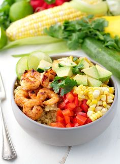 a bowl filled with shrimp, corn and avocado on top of a table