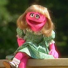 a pink stuffed animal sitting on top of a wooden table next to a green dress