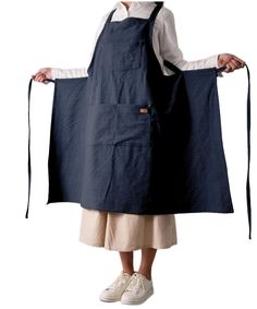 a woman wearing a blue apron and white shirt is standing with her hands in the pockets