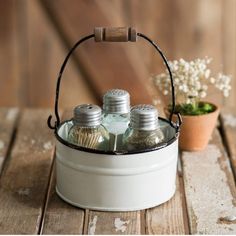 a white bucket with three bottles in it sitting on a wooden table next to a potted plant