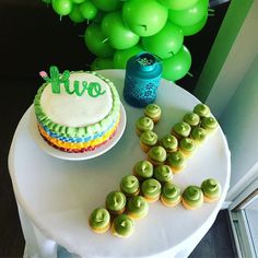 a table topped with a cake and cupcakes next to green balloons in the air