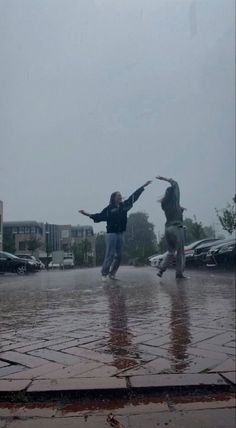 two people jumping in the air on a rainy day with their arms spread wide open