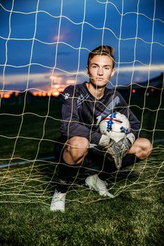 a soccer goalie sitting in front of the net holding a ball and looking at the camera