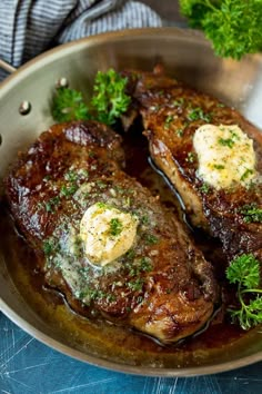 two steaks in a pan with butter and parsley on the top, ready to be eaten