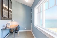 an empty room with a desk and large window overlooking the ocean on a sunny day