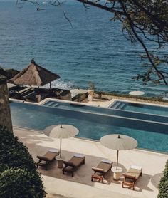 an outdoor swimming pool with lounge chairs and umbrellas next to the water's edge