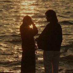 two people are standing on the beach near the water and birds flying in the sky