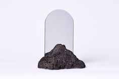 a large mirror sitting on top of a rock next to a pile of dirt in front of a white background