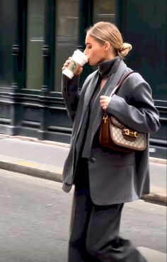 a woman walking down the street while holding a coffee cup in one hand and a purse in the other