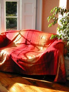 the couch is covered with a red cover in front of an open window and potted plant