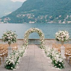 an outdoor ceremony set up with flowers and greenery on the side of a body of water