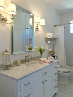 a white bathroom with marble counter tops and vanity lights above the sink, along with a large mirror on the wall