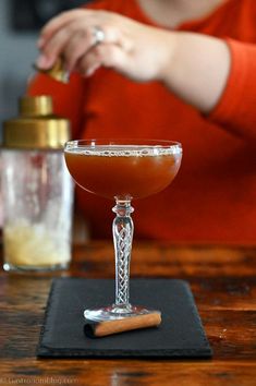 a woman sitting at a table with a drink in a glass on top of it