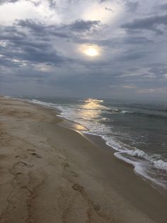 the sun is setting over the ocean with footprints in the sand and waves crashing on the beach