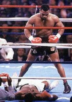 two men in the ring with one laying on the ground and another standing over him