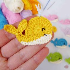 a small crocheted yellow fish sitting on top of a persons hand in front of some other knitted items