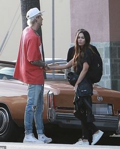 a man standing next to a woman in front of a brown car on the street