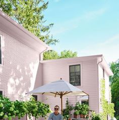 a man standing under an umbrella in front of a pink house with potted plants