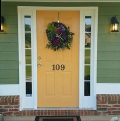 a yellow front door with a wreath on it and the number 1909 written in black