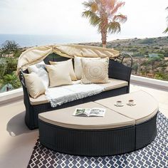 a couch with pillows on top of it near a palm tree and ocean in the background