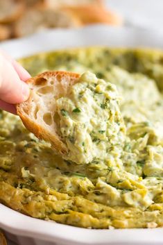 a hand dipping a piece of bread into a bowl of guacamole dip