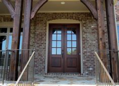 the front entrance to a brick house with double doors and wooden beams on each side