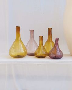 five different colored vases sitting on top of a white shelf next to each other