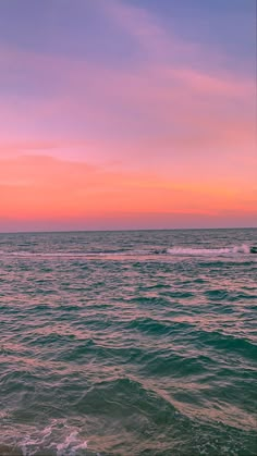 the sun is setting over the ocean with waves coming in to shore and a boat out on the water