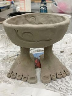 a cement bowl sitting on top of a table next to a pair of feet that are sticking out of it