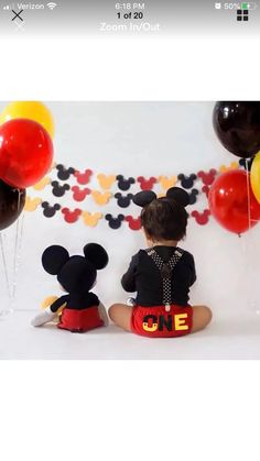 a little boy sitting on the floor with balloons and mickey mouse decorations in front of him