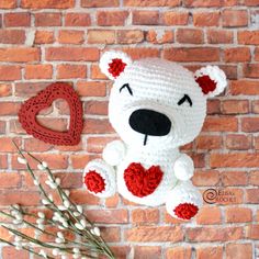 a crocheted teddy bear sitting next to a heart shaped object on a brick wall