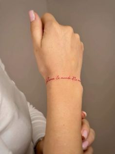 a woman wearing a white shirt holding her arm with a red tattoo on it's wrist