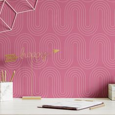 a pink wallpaper with the words happy written on it in gold foil next to a white desk