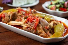 a white dish filled with meat and vegetables on top of a wooden table next to other dishes