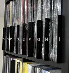 a book shelf filled with lots of books and vinyl records next to a wall that says abc def g h i