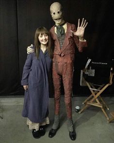 two people standing next to each other in front of a black backdrop with an alien statue