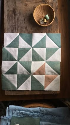 a wooden table topped with a basket filled with green and white quilted squares on top of it