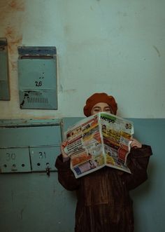 a woman in a brown dress and hat holding up a bunch of newspapers to her face