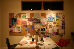 a room with a table and chairs covered in art work on the wall next to two windows