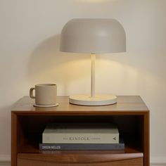 a white lamp sitting on top of a wooden table next to a cup and books