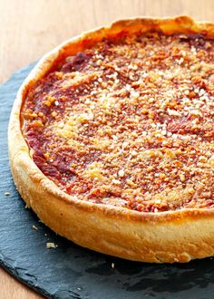 a pizza sitting on top of a wooden table next to a black slate plate with a crusty topping