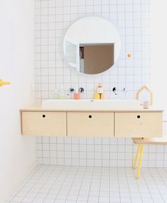 a white tiled bathroom with a wooden vanity and mirror above the sink, along with yellow stools