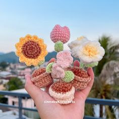 hand holding crocheted flowers on top of a balcony