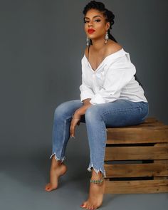 a woman sitting on top of a wooden box wearing jeans and a white off the shoulder shirt