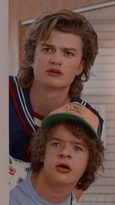 two young boys wearing baseball caps in front of a door with the same hat on their head