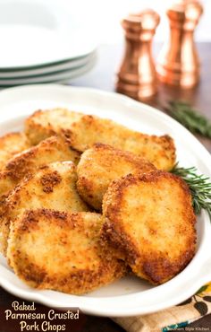 fried pork chops on a white plate with rosemary sprigs and two copper pepper shakers in the background