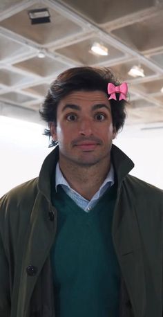 a man with a pink bow on his head looking at the camera while wearing a green jacket