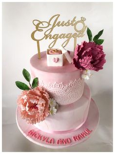 a wedding cake with pink and white flowers on the top is decorated with gold lettering that says just engaged